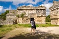 Woman tourist in black hat and shorts stands in front of the remains of a temple at Chichen Itz