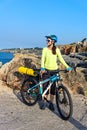 Woman tourist cyclist on the rocky shore on the lighthouse background