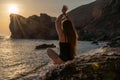 Woman tourist enjoying sunset over the sea mountain landscape. Sits outdoors on a rock above the sea. She is wearing Royalty Free Stock Photo