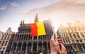 Woman tourist holds in her hand a flag of Belgium against the background of the Grand-Place Square in Brussels, Belgium