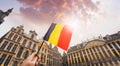 Woman tourist holds in her hand a flag of Belgium against the background of the Grand-Place Square in Brussels, Belgium