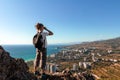 Woman tourist looking through binoculars at distant sea and city, enjoying landscape