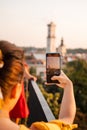 woman tourist looking at city on sunset from observation deck taking picture on her phone