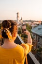 woman tourist looking at city on sunset from observation deck taking picture on her phone