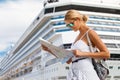 Woman tourist with map, standing in front of big cruise liner, travel female