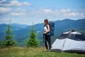 Woman tourist near camping in the mountains with backpack and trekking sticks in the morning Royalty Free Stock Photo