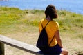 Woman tourist sitting on wooden bench looks sea atlantic ocean on walk beach summer tour with backpack Royalty Free Stock Photo