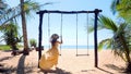 Woman tourist swinging on swing on sandy beach with palm trees and blue sea Royalty Free Stock Photo