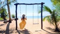 Woman tourist swinging on swing on sandy beach with palm trees and blue sea Royalty Free Stock Photo