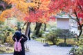 Woman tourist taking photo colorful leaves by camera in Tenryuji temple at Arashiyama, young Asian traveler visit in Kyoto, Japan