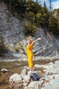 Woman tourist walking by mountain river enjoying landscape. Traveler feels happy raising arms. Summer vacation