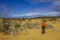 A woman tourist walks through The Pinnacles formation under clear, blue sky at Nambung National Park in Western Australia.