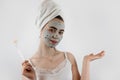 woman in towel with brush applied a black cleansing mask on face isoalted on white