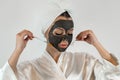 woman in towel with brush applied a black cleansing mask on face isoalted on white