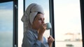 Woman with towel on head drinking coffee in background of window. Concept. Beautiful young woman preparing for start of