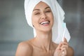 Woman with towel on head holding toothbrush looking at camera