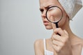 woman with a towel on her head holds a magnifying glass near face skin problems pimple
