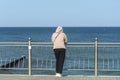 Woman in tracksuit stands with her back on seashore and looks into distance. Concept of waiting, farewell to sea. Selective focus