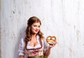 Woman in traditional bavarian dress holding pretzel, wooden back Royalty Free Stock Photo