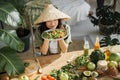Woman in traditional conical hat holding salad from organic vegetables and fruit