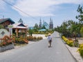 Woman with traditional hat walking in the street of Ngurbloat, a tiny colorful flowery village with a huge christian gotic style