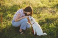 Woman training cute white puppy to behave and caressing him in summer meadow in warm sunset light. Adorable fluffy puppy kissing