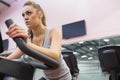 Woman in gray sleeveless top gripping handlebars and pedaling on cardio bike in gym, mirror visible Royalty Free Stock Photo