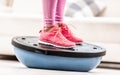 Woman in training shoes stands on a blue balance ball