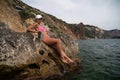 Woman travel sea. Pink bikini tourist captures sea memory, posing on beach amidst volcanic mountains for travel