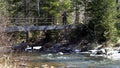 Woman traveler is on bridge over mountain river in spring. Media. Traveler crosses iron bridge over mountain river Royalty Free Stock Photo