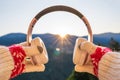 Woman traveler in christmas gloves holding headphones on top of mountains at morning sinrise with sunbeams. Winter travelling conc