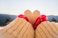 Woman traveler in christmas gloves holding snow in the shape of a heart on a background of mountains with sunbeams. Winter travell