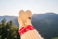 Woman traveler in christmas gloves holding snow in the shape of a heart on a background of mountains with sunbeams. Winter travell