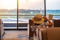 Woman traveler with hat looking to airplane in the morning sunrise, Asian passenger sitting and relax in modern lounge at