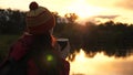 Woman Traveler holds metal mug with hot coffee in her hands and looks at the sunset by the river. free traveler girl