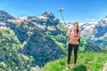 woman traveler photographing herself, making a salfi on the smartphone, against the backdrop of the mountain peaks of Switzerland Royalty Free Stock Photo