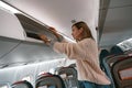 Woman traveler putting luggage into overhead locker on airplane during boarding