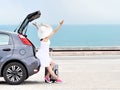 Woman traveler with raised arms on hatchback car on beach