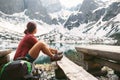 Woman traveler sits on rest point near mountain lake with beautiful view on snowy peaks