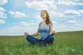 Woman traveler sitting on the meadow with green grass under blue sky with clouds in the Lotus position Royalty Free Stock Photo