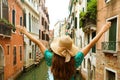 Woman traveler with straw hat and arms raised on bridge in Venice. Back view of fashion woman with open arms beautiful Venice