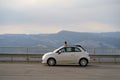 Woman traveller enjoys rocky landscapes above clouds high in mountains from small convertible car. Royalty Free Stock Photo