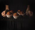 Woman with tray of vegan chocolate muffins, black background dark food