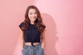 Woman in trendy garment smiling broadly and glancing at camera over pastel background