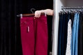 Woman trying on pants in a clothing store reaching out hand from a fitting room holding trousers Royalty Free Stock Photo