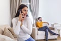 Woman turned her back to man, talking on phone with her lover, boyfriend sitting in the back watching tv. Cheating and infidelity Royalty Free Stock Photo