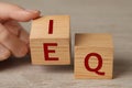 Woman turning cube with letters E and I near Q at wooden table, closeup