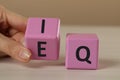 Woman turning pink cube with letters E and I near Q at white wooden table, closeup