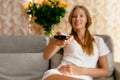 Woman with TV remote in hand watching TV while sitting on sofa at home Royalty Free Stock Photo
