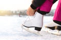 Woman tying ice skates laces by a lake or pond. Lacing iceskates. Skater about to exercise on an outdoor track or rink. Sunny win